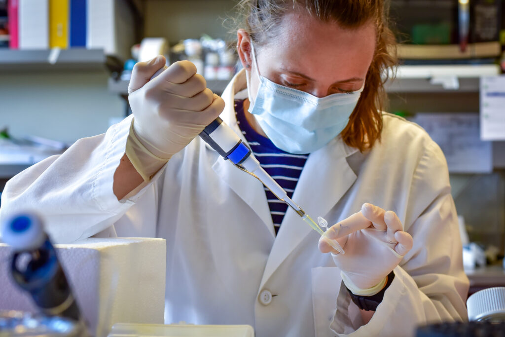 a person in a labcoat sitting at a bench and piping into a tube